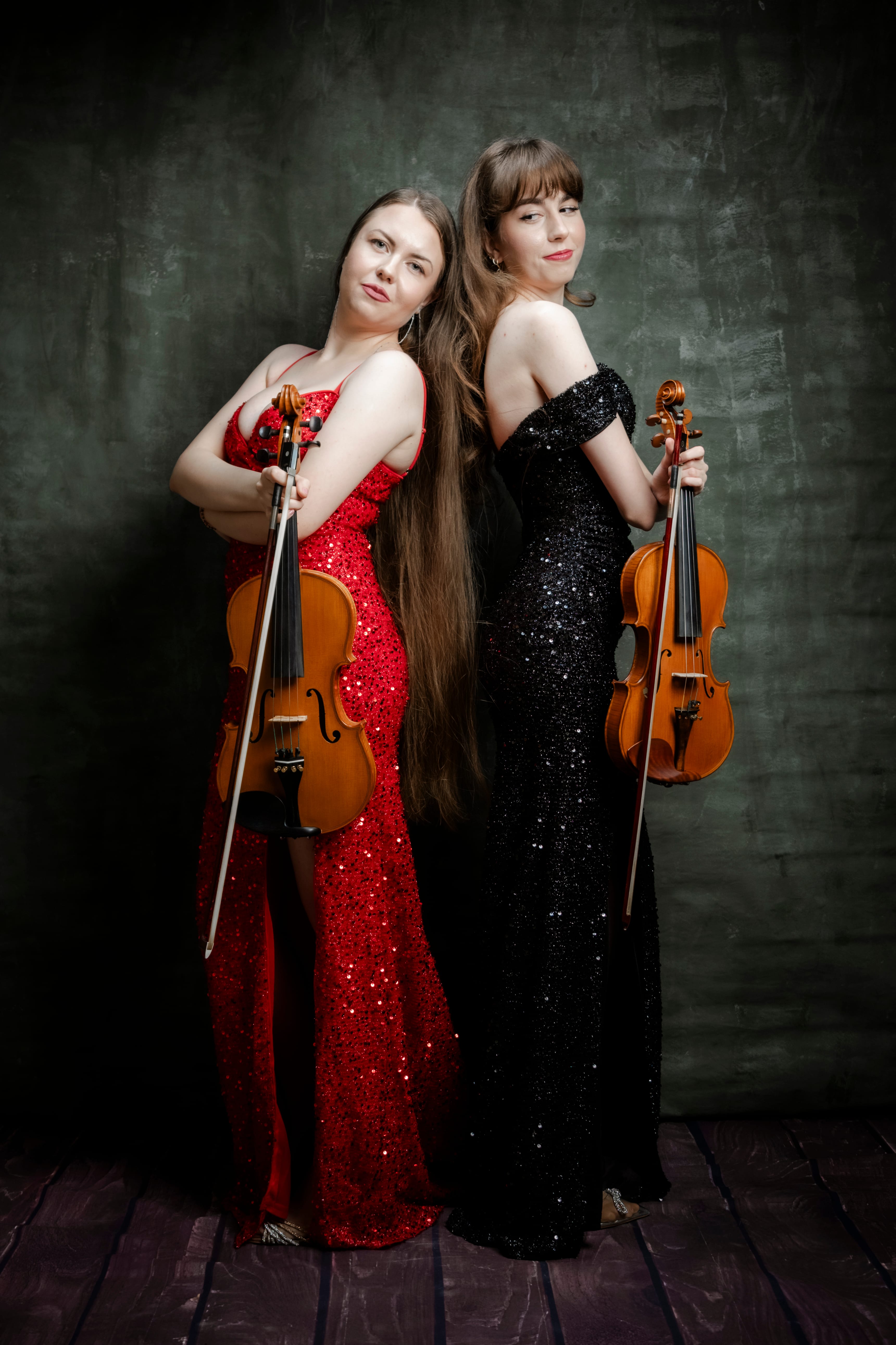 Sistrings duo standing back to back in red and black gowns holding violin and viola